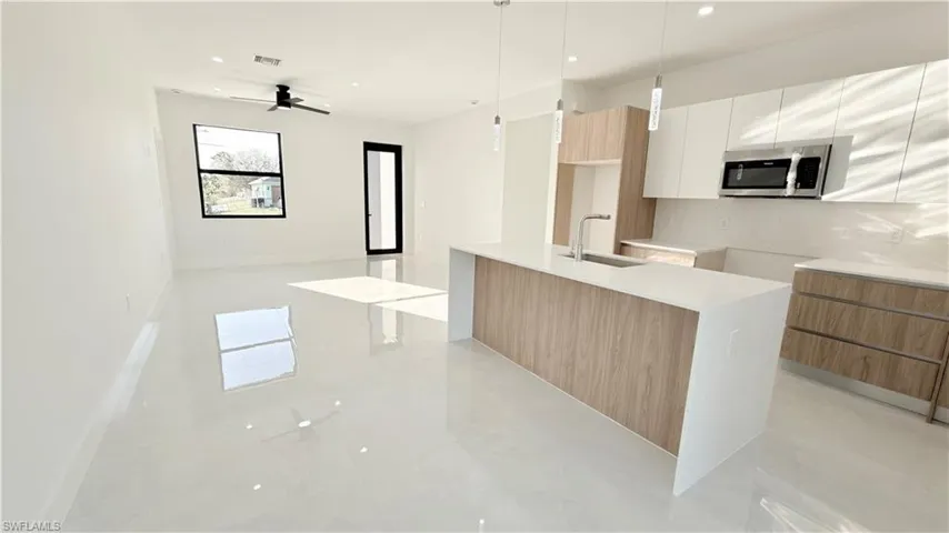Dual tone kitchen featuring modern cabinets, light stone countertops, two tone cabinetry, stainless steel microwave, and an island with sink