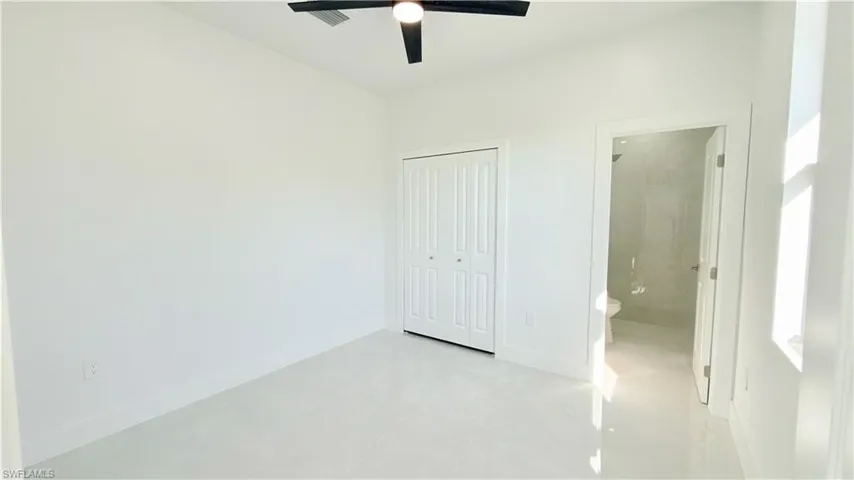 Unfurnished bedroom featuring ensuite bath, ceiling fan, and a closet