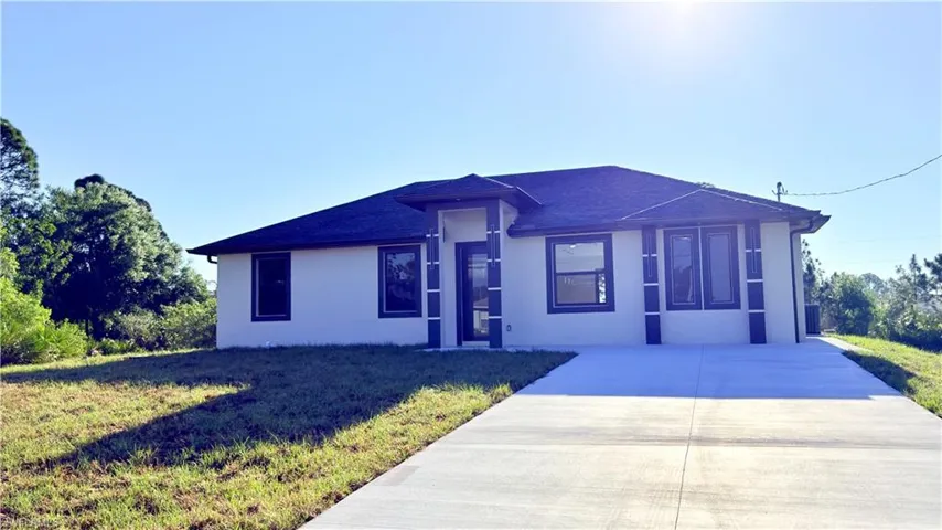 View of front of house with a front lawn, stucco siding, a shingled roof, and concrete driveway