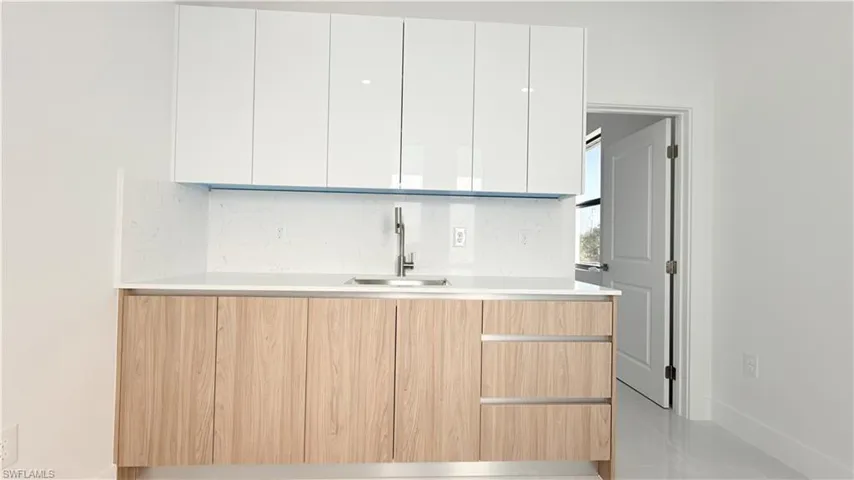 Kitchen with modern cabinets, backsplash, two tone cabinetry, and light stone counters