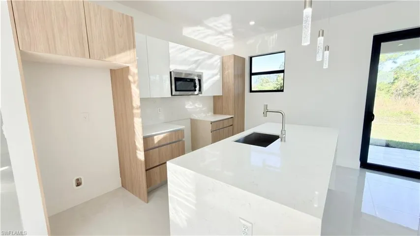 Kitchen featuring light stone counters, modern cabinets, two tone cabinetry, a kitchen island with sink, and hanging light fixtures