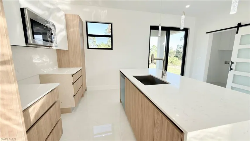Kitchen with modern cabinets, a barn door, light stone countertops, stainless steel appliances, and a center island with sink