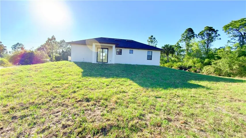 Rear view of property featuring a lawn and stucco siding
