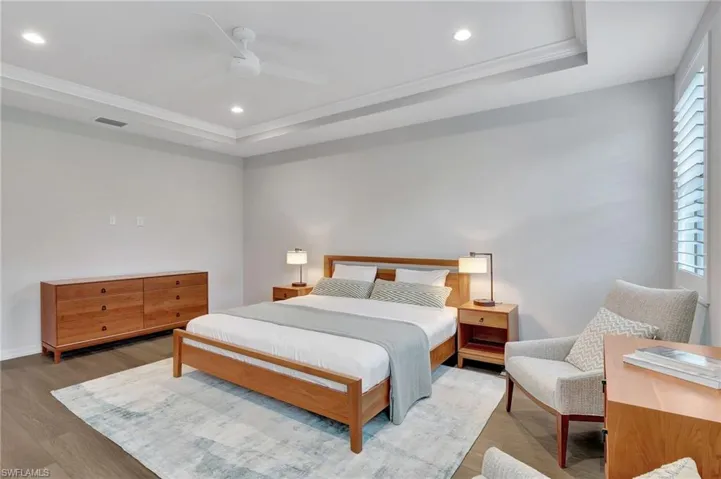 Bedroom with hardwood / wood-style floors, ceiling fan, a raised ceiling, and ornamental molding