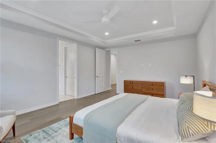 Bedroom with hardwood / wood-style flooring, ceiling fan, and a tray ceiling