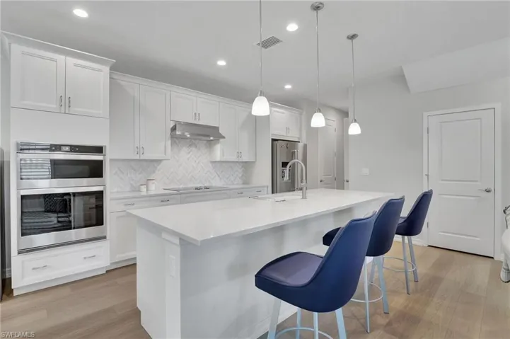 Kitchen with appliances with stainless steel finishes, a kitchen island with sink, sink, pendant lighting, and white cabinetry