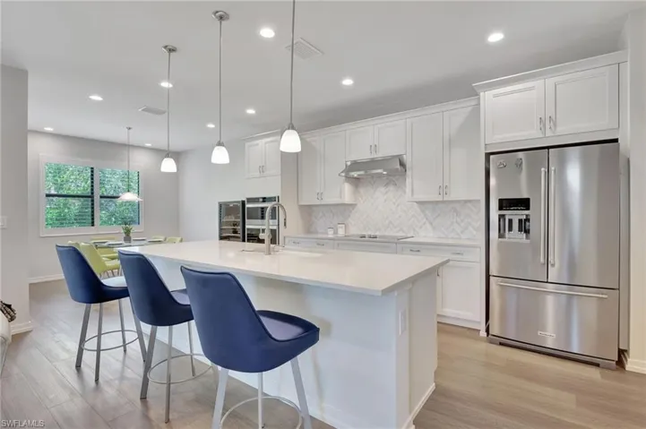 Kitchen with sink, stainless steel appliances, an island with sink, decorative light fixtures, and white cabinets
