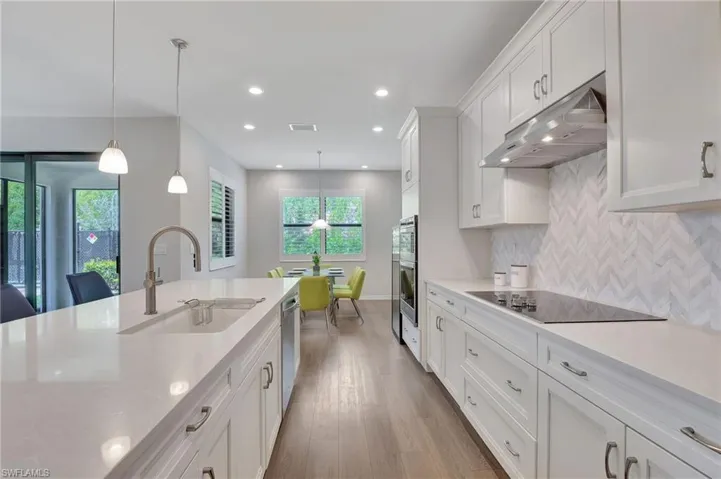 Kitchen with sink, pendant lighting, black electric cooktop, decorative backsplash, and white cabinets