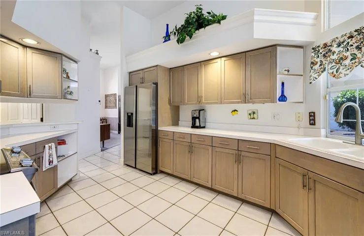 Kitchen with open shelves, a high ceiling, a sink, light countertops, and stainless steel fridge