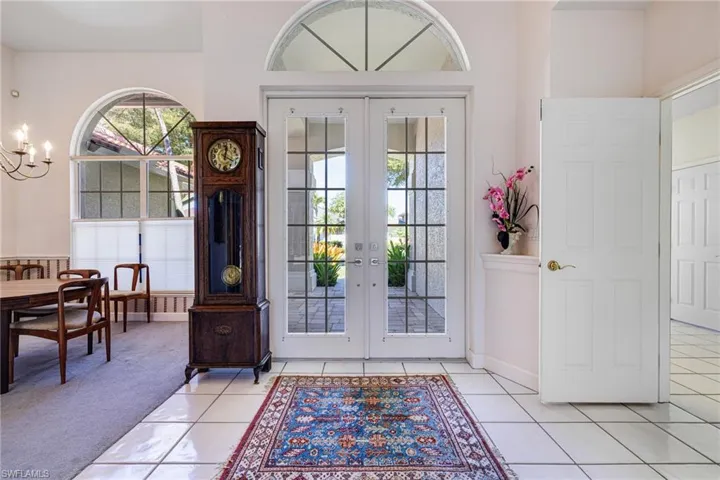 Foyer entrance with french doors, light colored carpet, light tile patterned flooring, and a notable chandelier