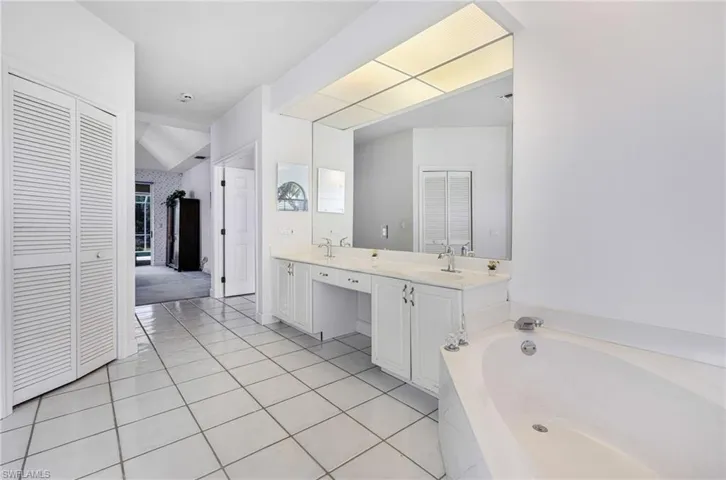 Bathroom with tile patterned flooring, a garden tub, double vanity, a closet, and a sink