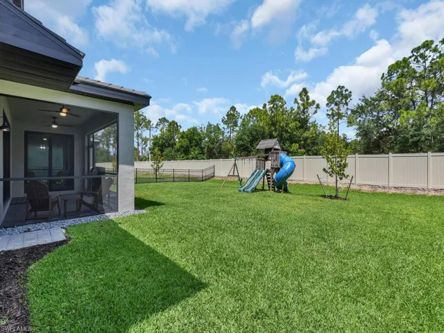 The property features a spacious lawn, a screened-in patio with a ceiling fan, and a light-toned privacy fence in addition to black metal fence around the back