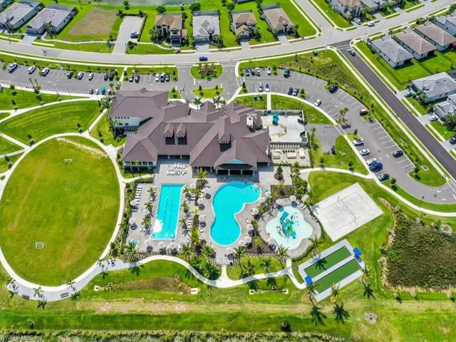 Aerial view of the property's recreational facilities, featuring a large clubhouse, two swimming pools, a sports field, a sand volleyball court, and bocce ball courts