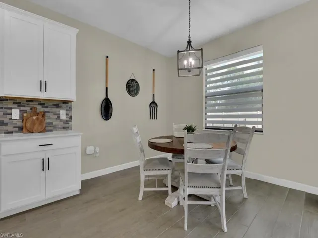 This dining area features light-colored walls and flooring, with a window providing natural light