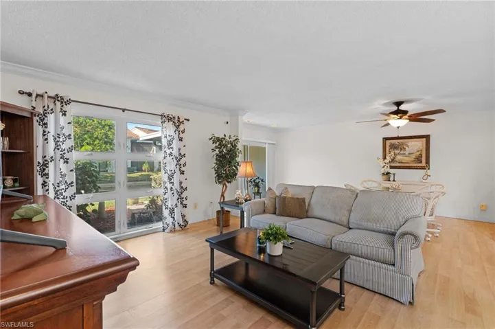 Living room featuring light wood finished floors, a ceiling fan, a textured ceiling, and crown molding