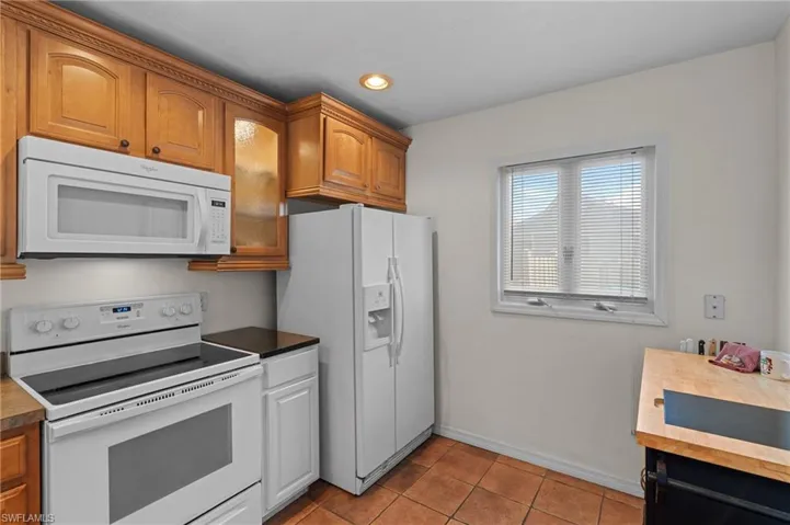Kitchen featuring white appliances, light tile patterned flooring, dark countertops, glass insert cabinets, and recessed lighting