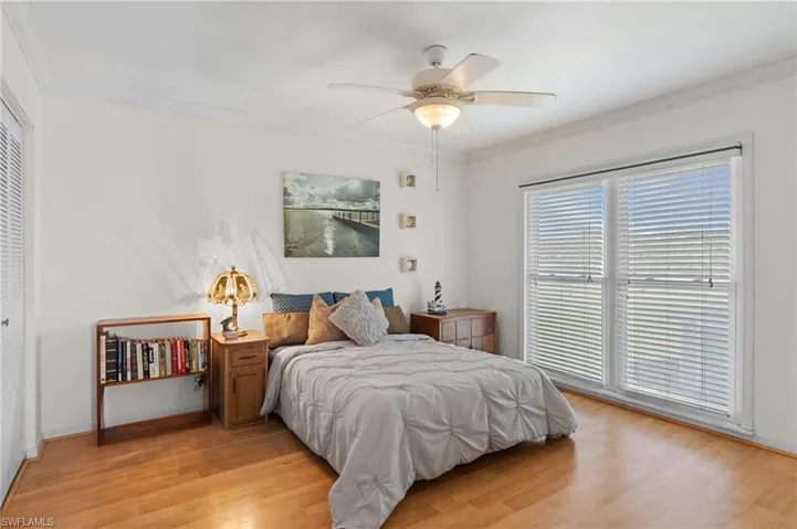 Bedroom featuring crown molding, light wood-style flooring, a ceiling fan, and a closet