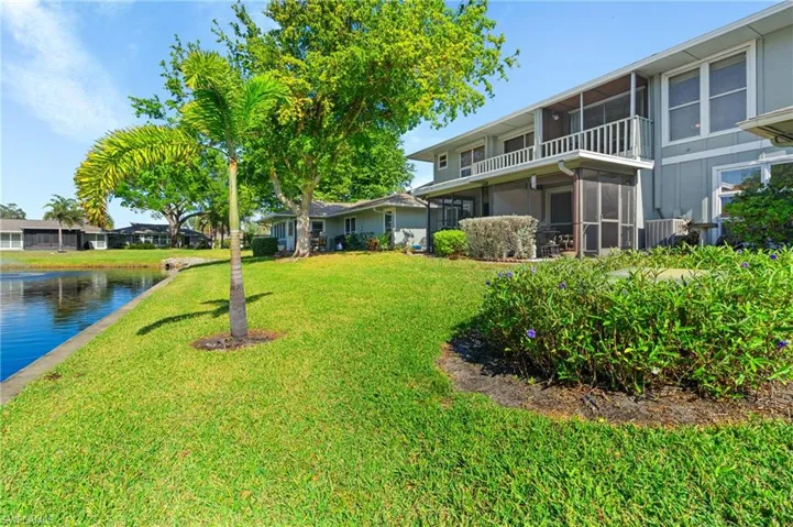 View of green lawn with a sunroom, a balcony, and a water view
