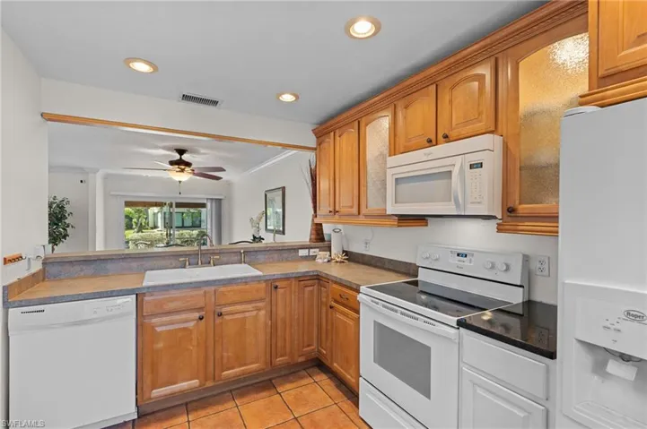 Kitchen featuring white appliances, light tile patterned flooring, ornamental molding, brown cabinets, and recessed lighting
