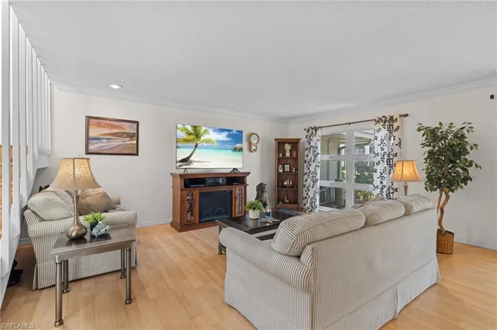 Living room with light wood-type flooring, a fireplace, recessed lighting, and crown molding