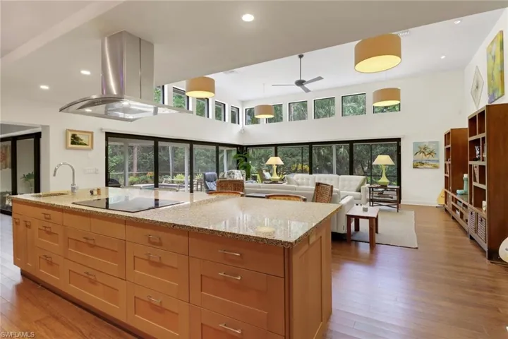 Kitchen with island range hood, wood finished floors, light stone countertops, ceiling fan, and recessed lighting