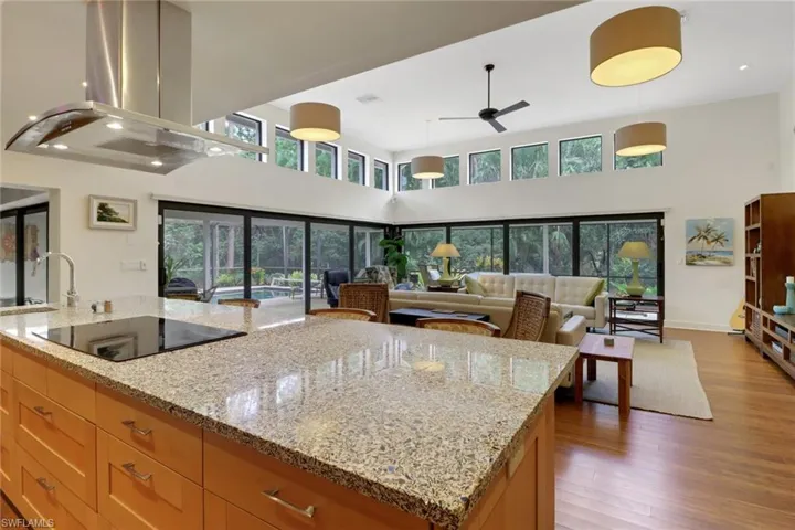 Kitchen with island range hood, a high ceiling, ceiling fan, wood finished floors, and black electric cooktop