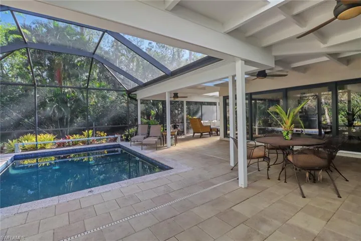 Swimming pool featuring ceiling fan, a patio, outdoor dining area, and glass enclosure