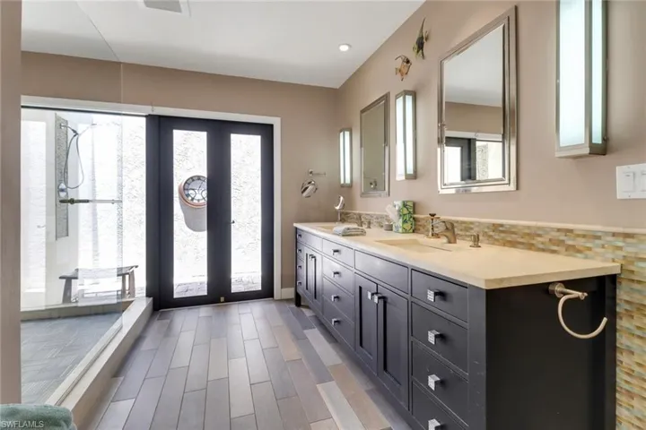 Primary Bathroom, custom wood cabinets, travertine vanities, mirrors and lighting, frameless shower enclosureimpact French leading outdoor shower