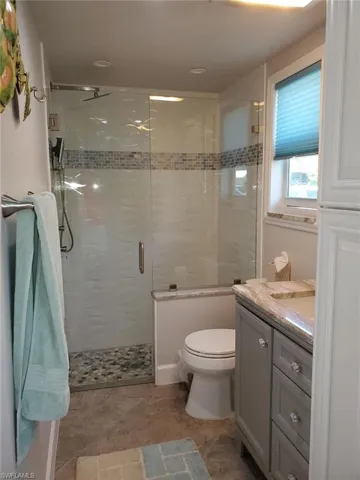 Bathroom featuring tile patterned flooring, toilet, a shower with door, and vanity