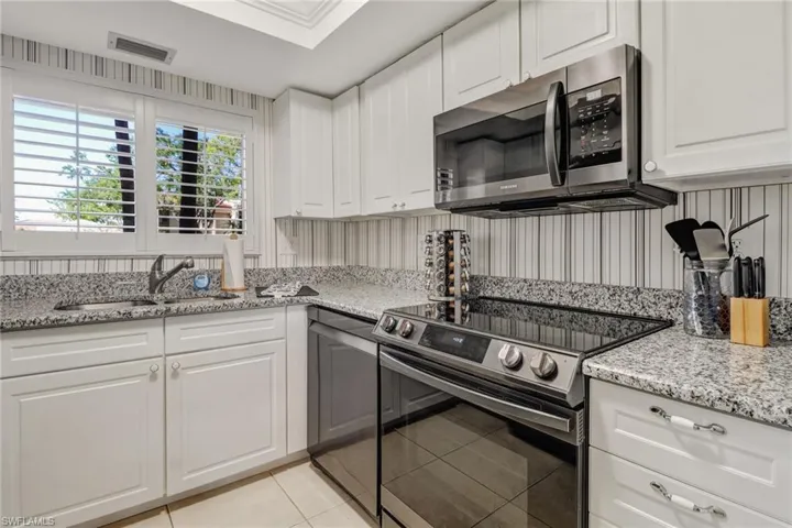 Kitchen with stainless steel appliances, sink, light stone counters, light tile patterned floors, and white cabinetry