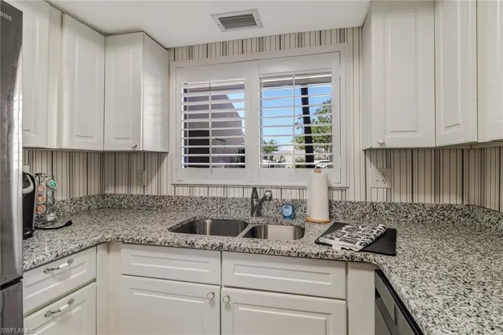 Kitchen with sink, white cabinetry, light stone counters, and stainless steel fridge
