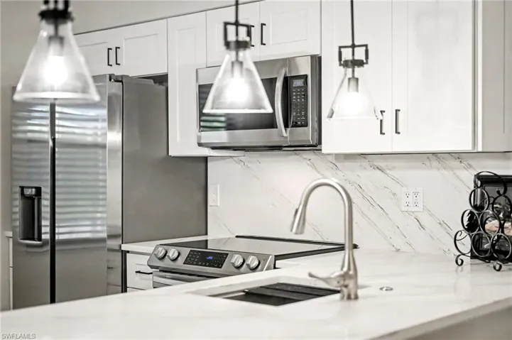 Kitchen with stainless steel microwave, white cabinetry, light stone counters, and tasteful backsplash