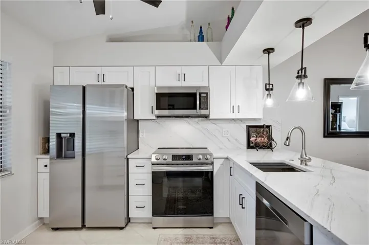 Kitchen with stainless steel appliances, white cabinets, light stone countertops, decorative light fixtures, and vaulted ceiling
