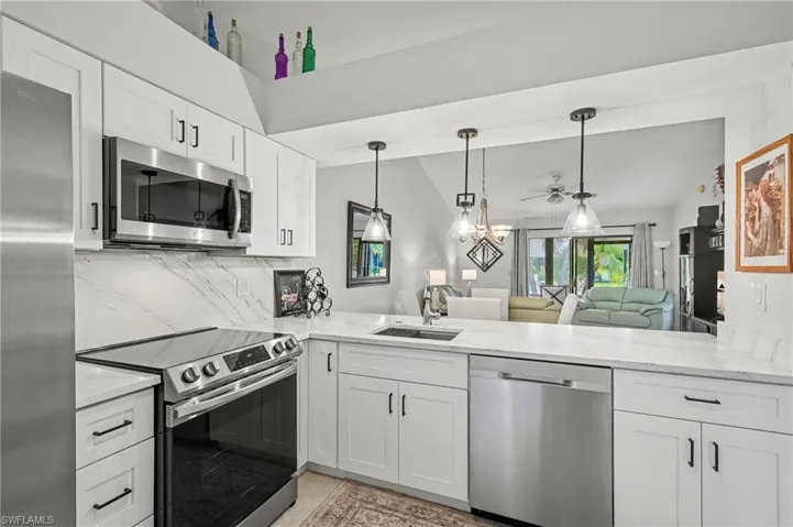 Kitchen featuring stainless steel appliances, white cabinets, open floor plan, light stone countertops, and a peninsula