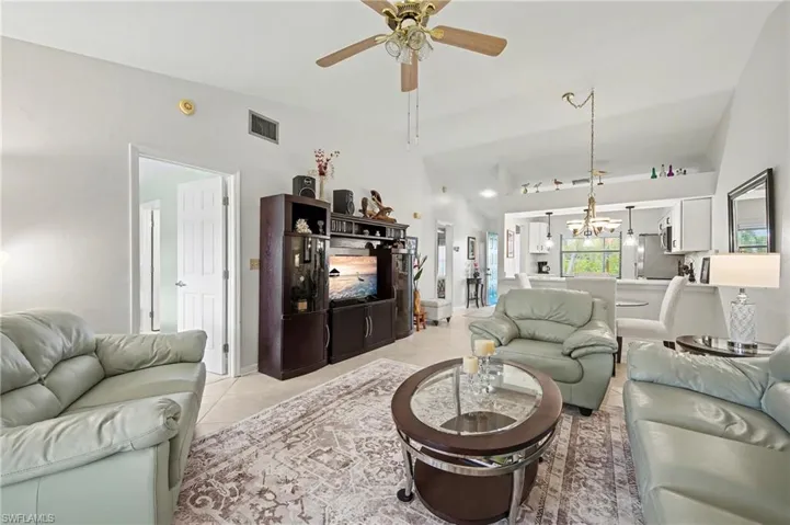 Living room featuring vaulted ceiling, light tile patterned flooring, a ceiling fan, and a chandelier