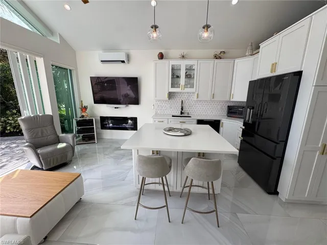 Kitchen with white cabinetry, black appliances, a wall mounted AC, hanging light fixtures, and lofted ceiling