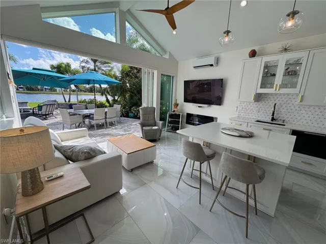 Living room with a water view, a wall mounted AC, sink, high vaulted ceiling, and ceiling fan