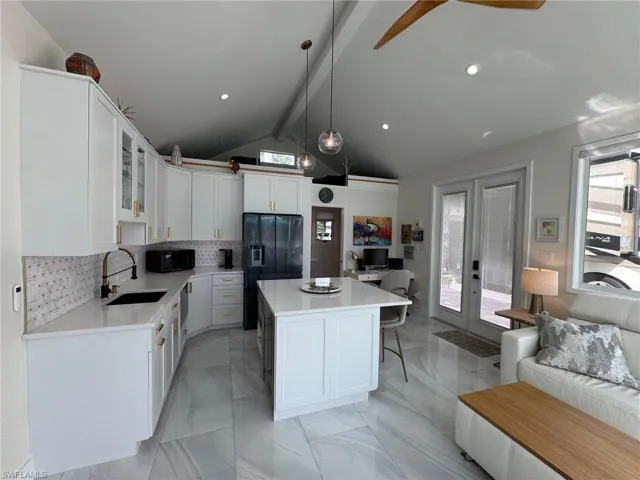 Kitchen with black fridge with ice dispenser, decorative light fixtures, a kitchen island, and plenty of natural light