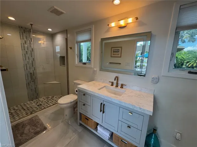 Bathroom featuring toilet, vanity, and a shower with door