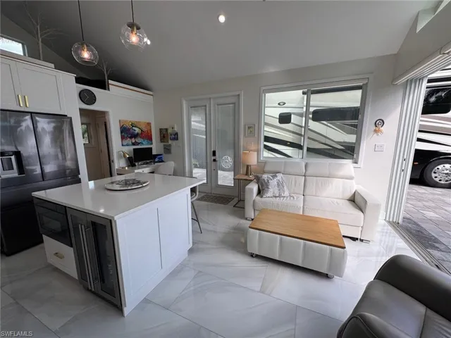 Kitchen with lofted ceiling, black fridge with ice dispenser, a kitchen island, pendant lighting, and white cabinetry
