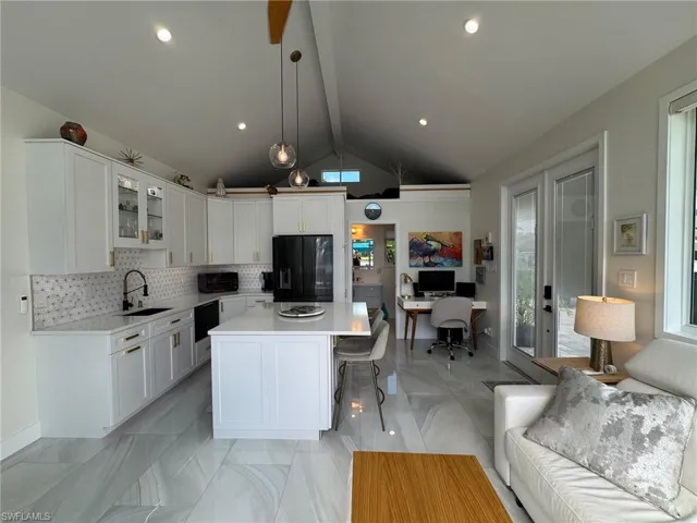 Kitchen featuring lofted ceiling with beams, black fridge, a kitchen island, white cabinetry, and sink