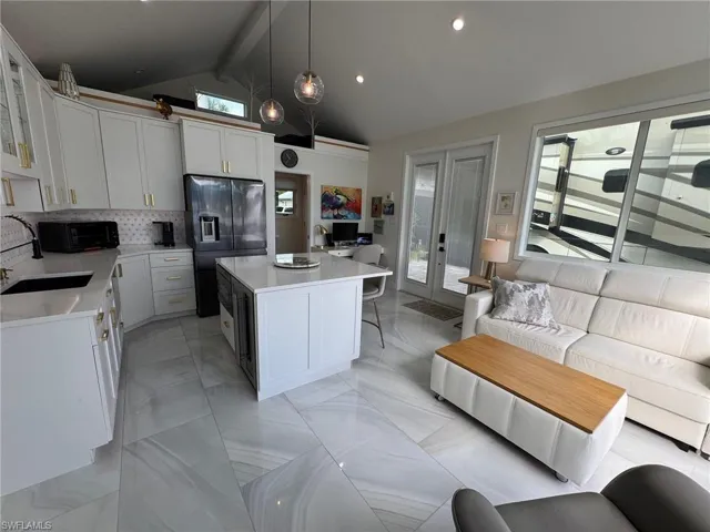 Kitchen with stainless steel fridge, a kitchen island, white cabinetry, beam ceiling, and hanging light fixtures