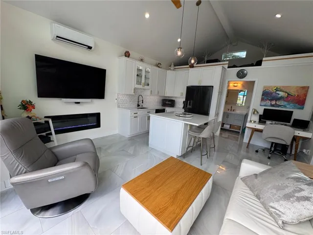 Tiled living room with a wall mounted AC, beam ceiling, sink, and high vaulted ceiling