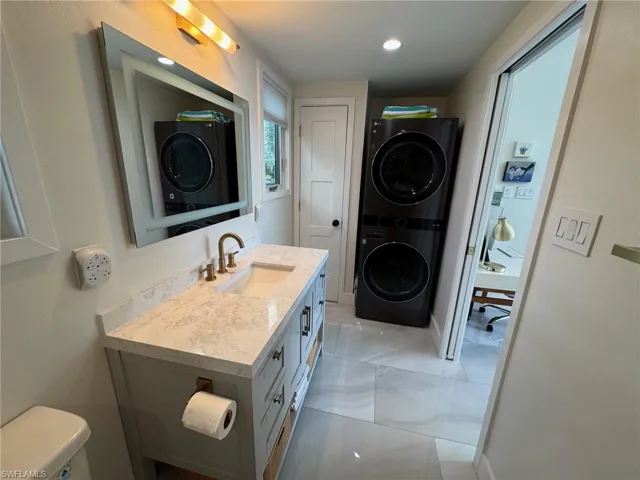 Bathroom with toilet, stacked washing maching and dryer, and sink