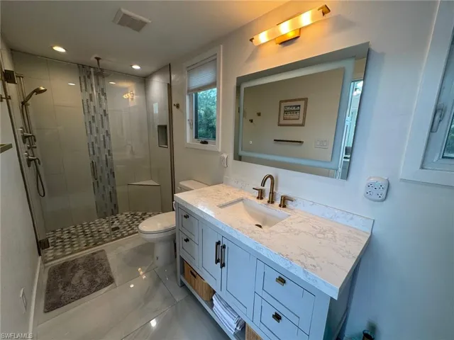 Bathroom with toilet, vanity, and a shower with shower door