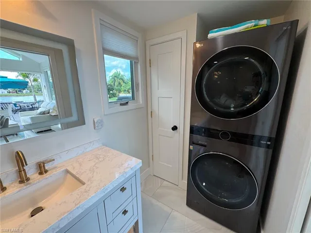 Clothes washing area with stacked washing maching and dryer, sink, light tile patterned floors, and plenty of natural light