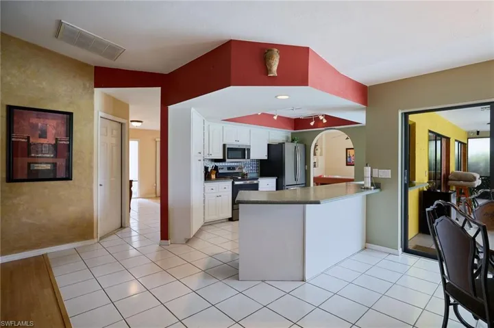 Kitchen featuring stainless steel appliances, a peninsula, white cabinetry, arched walkways, and light tile patterned floors