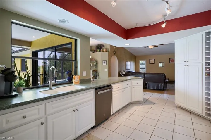 Kitchen with stainless steel dishwasher, white cabinets, light tile patterned floors, and ceiling fan