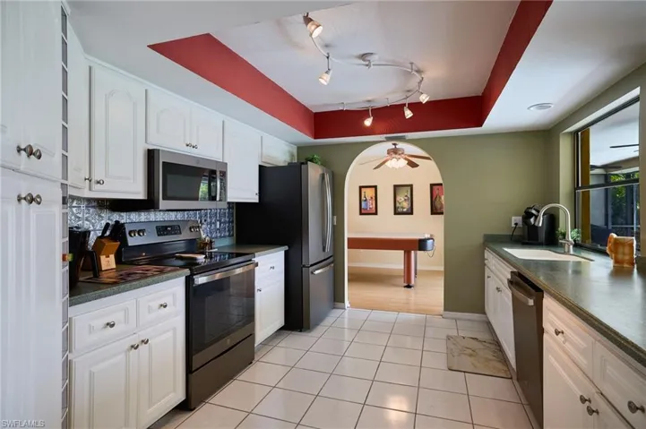 Kitchen featuring stainless steel appliances, dark countertops, white cabinets, tasteful backsplash, and light tile patterned floors
