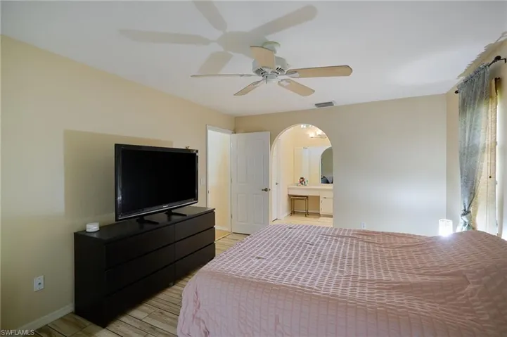 Bedroom with arched walkways, light wood-type flooring, ensuite bath, and a ceiling fan